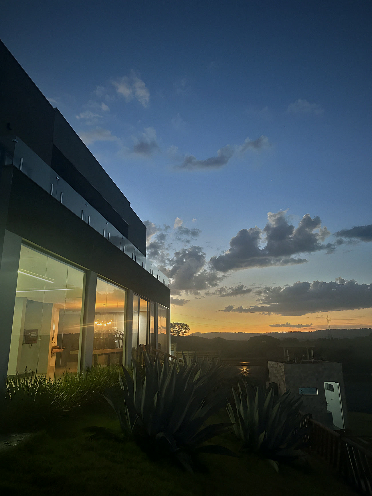 Casa de vidro com nuvens douradas no pôr do sol da serra